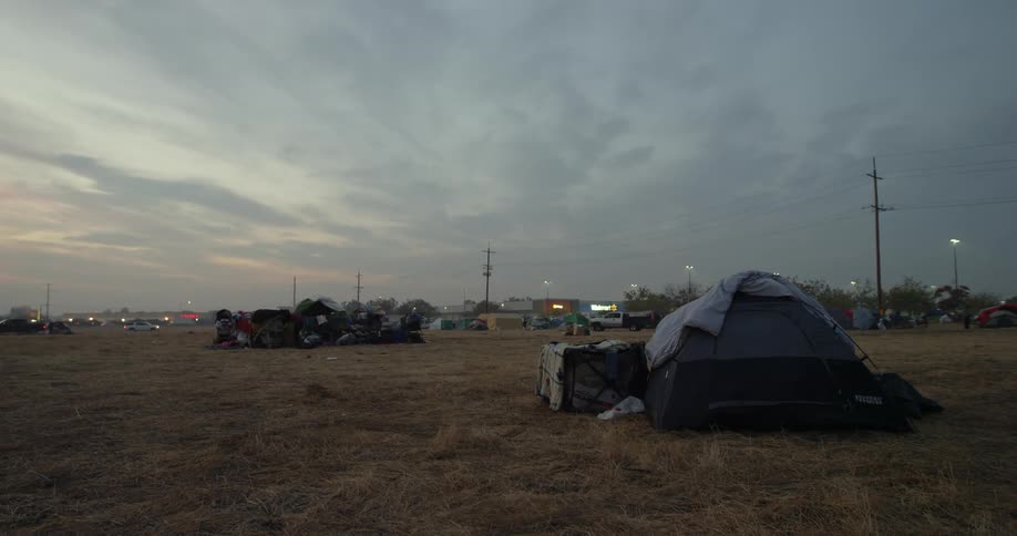 Tents are set up in an open field for people who lost their homes in the Paradise fire disaster behind them the stores in a small strip mall and the vehicles passing by