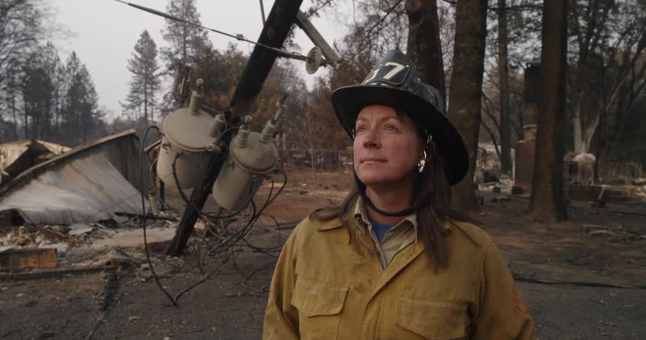 A firefighter stands in front of a burned down power pole in the woods