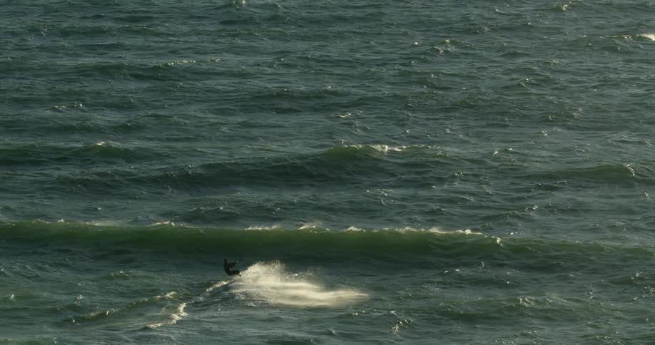 Aerial view of a person kitesurfing on backlite waves in the ocean