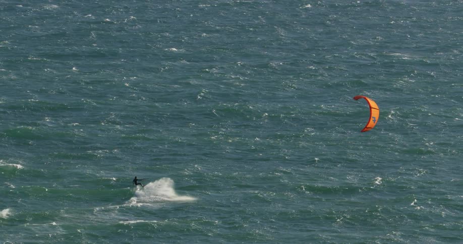 People are kitesurfing in the ocean on a sunny and windy day