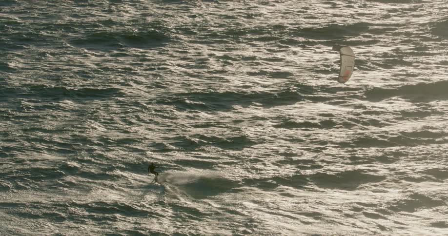 A man is skillfully kitesurfing through a vast ocean with nothing but the endless blue water stretching out in all directions around him