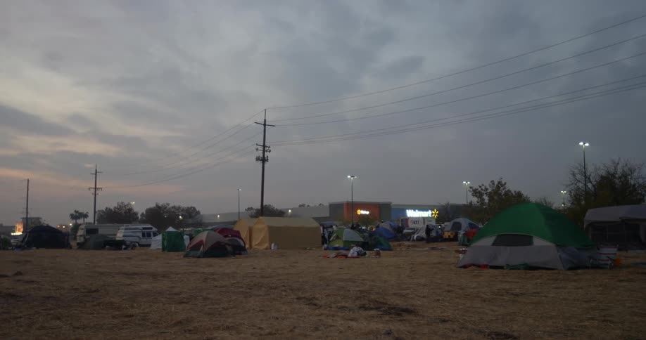 Pitched tents in an open field for people who lost their homes in the Paradise fire disaster behind them the stores in a small strip mall