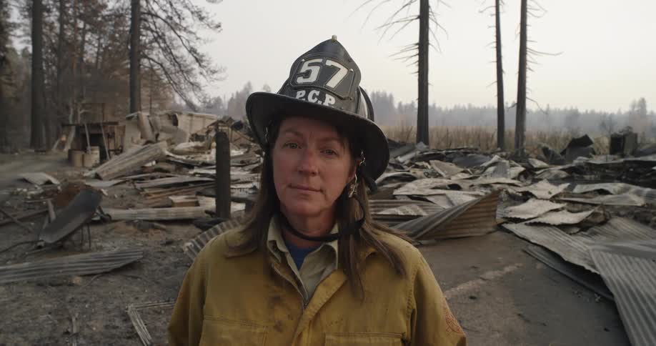 Female fire fighter standing in front of fire damaged rural area