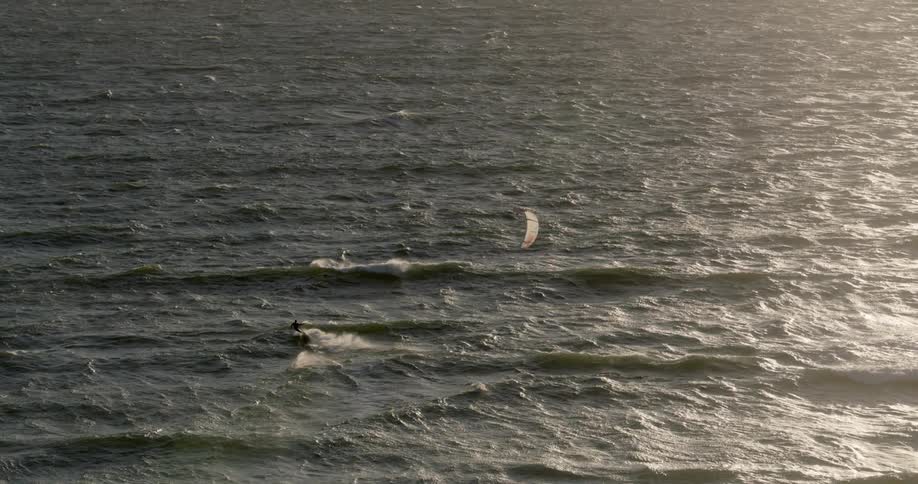 A person kitesurfs through the waves of the open ocean at sunset