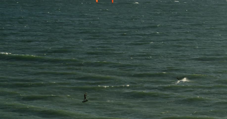 People are kitesurfing and jumping off waves in the ocean