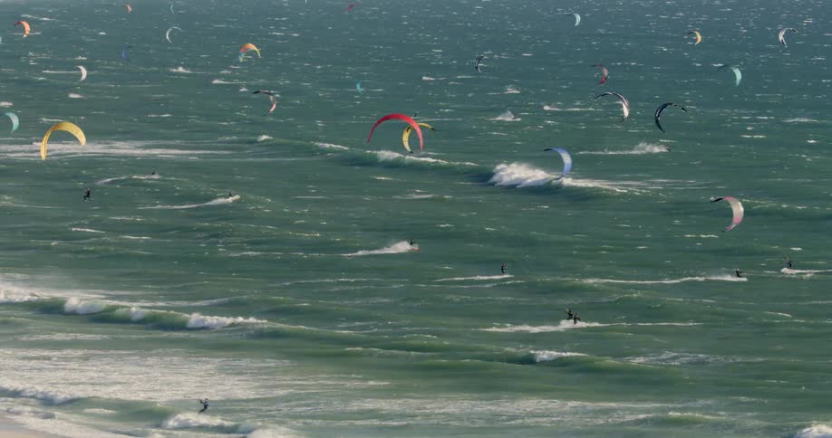 Large group of kitesurfers sailing in the waves at Blouberg Beach on a sunny day