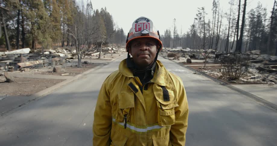 Male firefighter stands in road between remains of burned down buildings