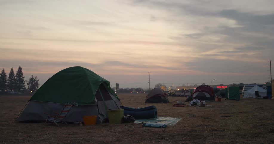 Tents are set up for people who lost their homes in the Paradise fire disaster behind them the stores in a small strip mall and the vehicles passing by have their lights on