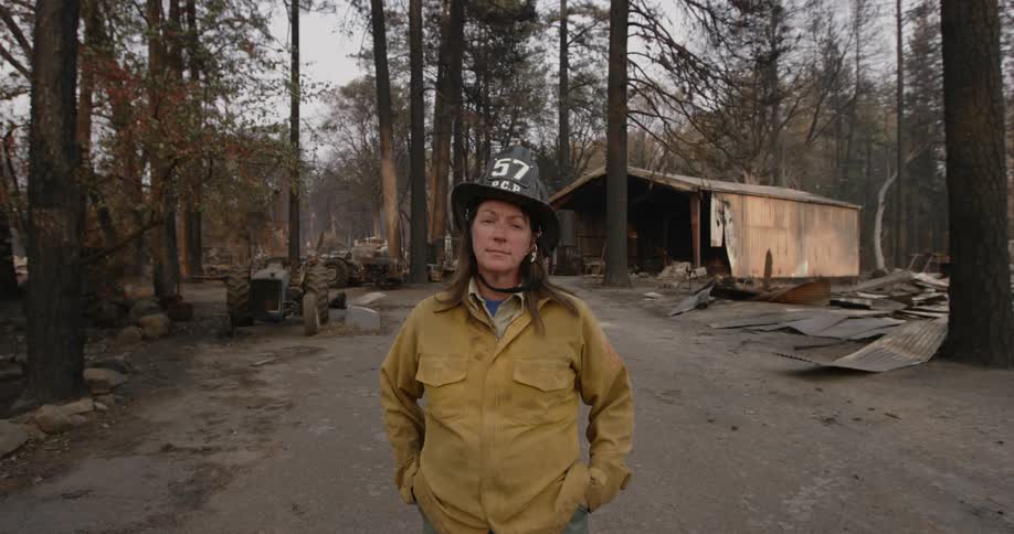A firefighter stands in front of a burned down cabin in the woods