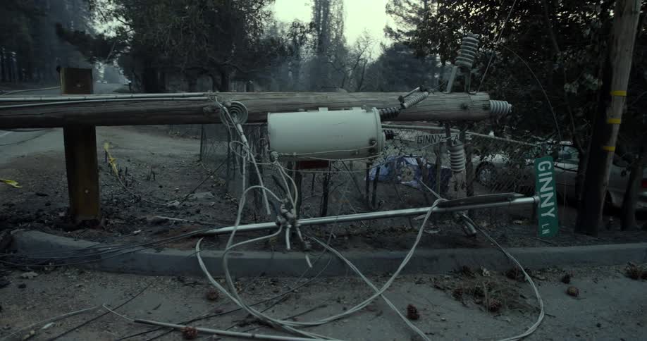 A utility pole and street sign are lying on the side of the road with electrical cables stretching across the asphalt