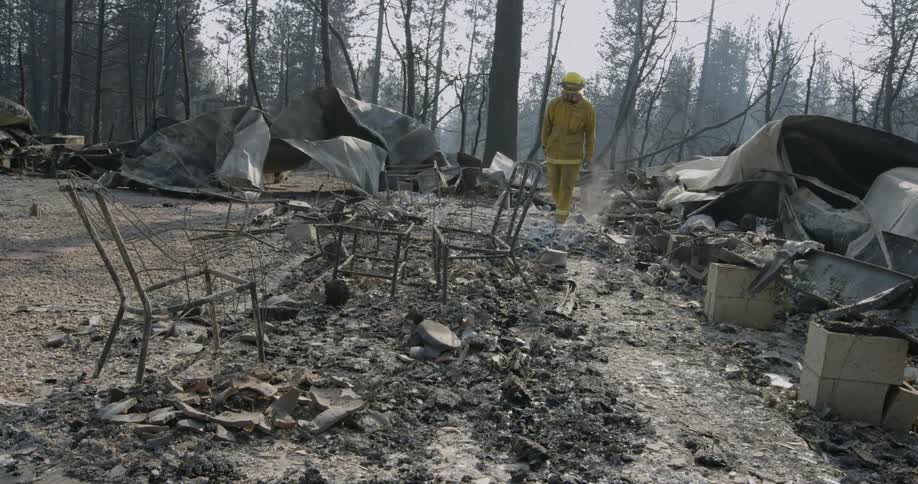 Firefighter walking through the debris while holding an axe in the aftermath of a fire in the forest
