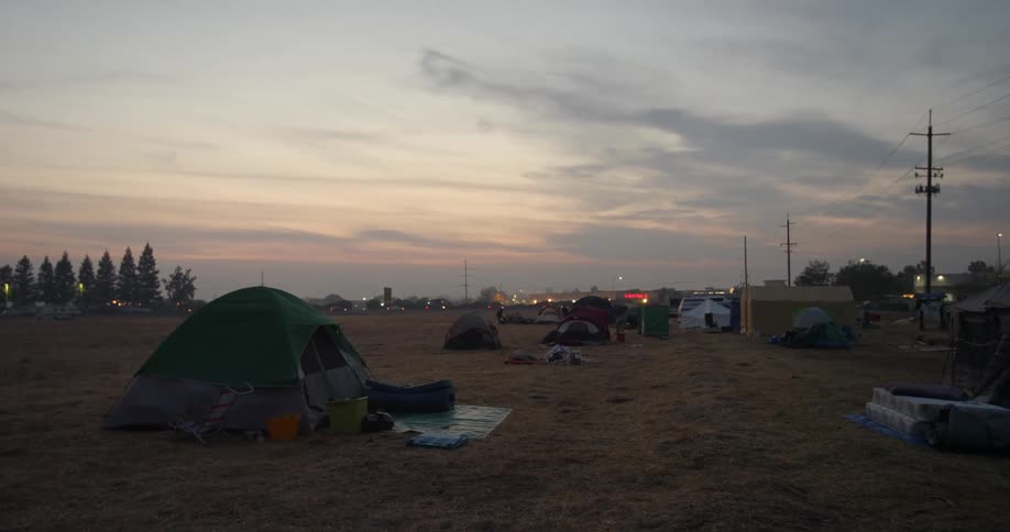 Tents are pitched in an open field for people who lost their homes in the Paradise fire disaster behind them the stores in a small strip mall and the vehicles passing by