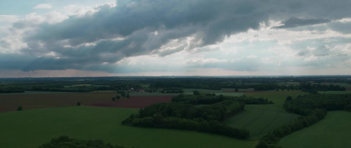 Rural town sits among fields stretching toward red tinted horizon under a heavily clouded sky