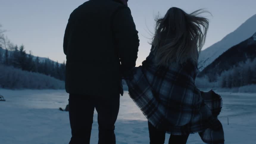 A man and woman running hand in hand on a frozen lake