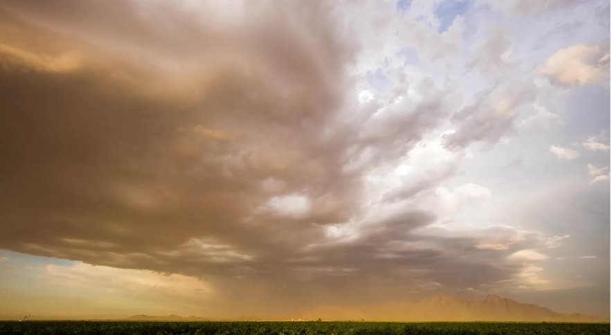 Storm clouds gather over fields near mountains and winds create dust storm