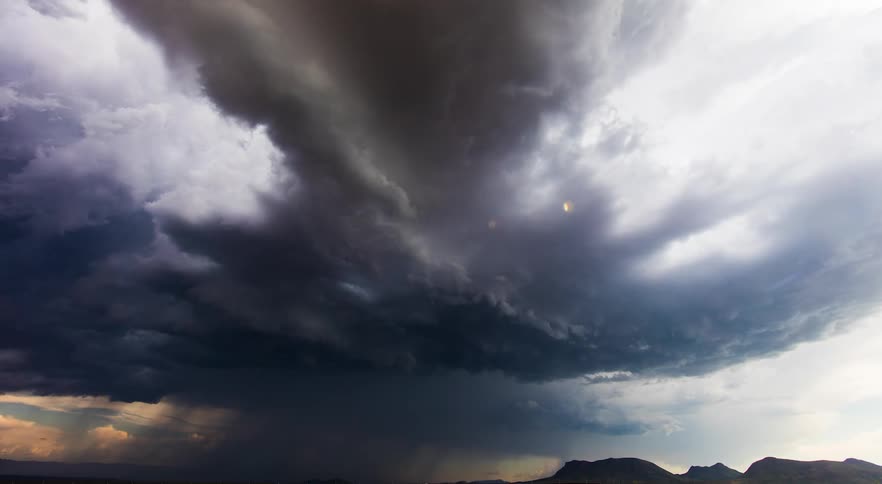 A wide landscape shot of a storm forming above a flat field