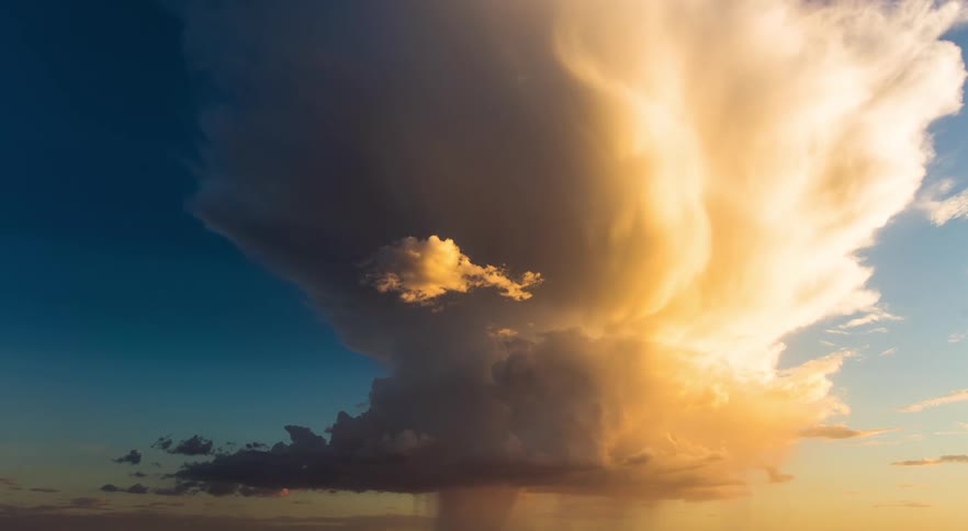 Sunlight is shining on large storm clouds that are flowing over and pouring rain on flatland