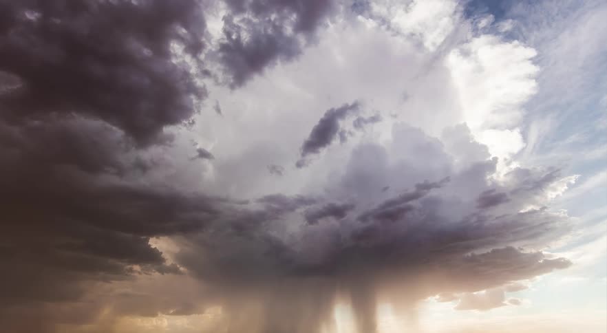 Dark storm clouds move across the sky as rain pours down from the clouds