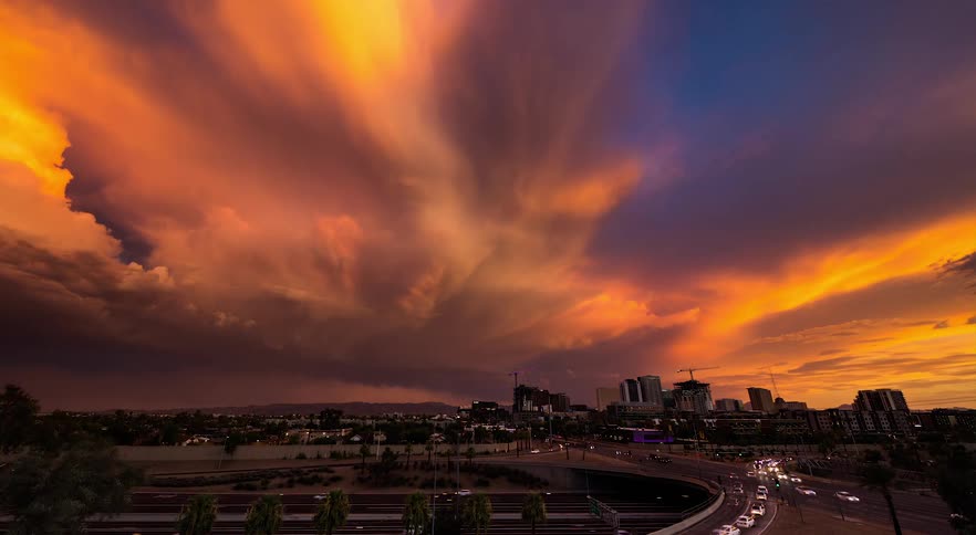 Traffic moves on busy highways and tall city buildings are on the skyline as bright clouds move over the city and the sky grows darker