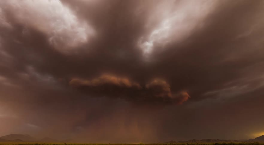 A dark severe thunderstorm with lightning and rain over the desert at sunset