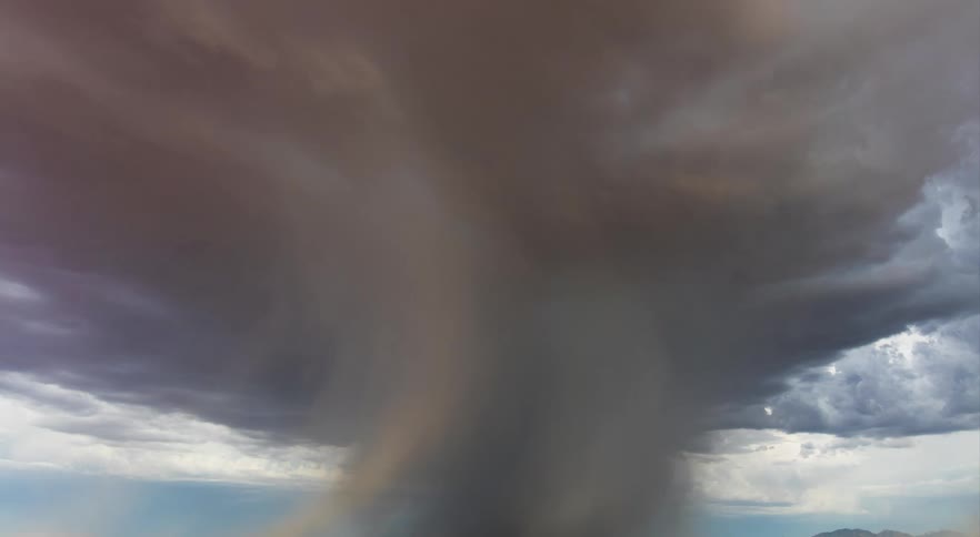 Lightning strikes through large dark storm cloud as it moves across arid scrub land near mountains