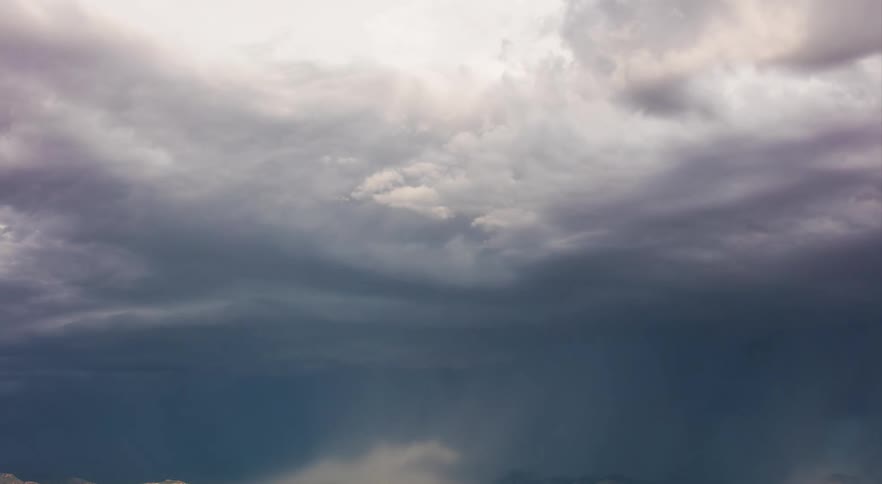 Dark storm clouds are moving in and pouring rain over a rural area