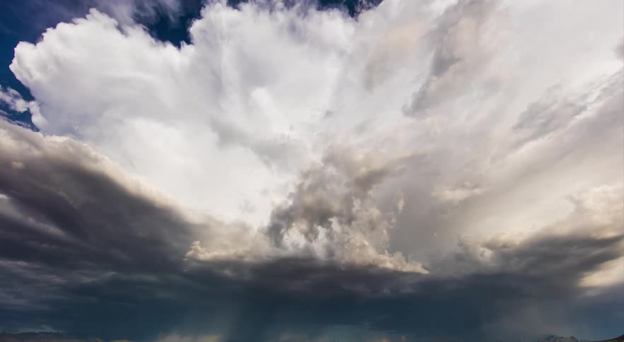 Bright white clouds move over rural land in a deep blue sky as dark clouds roll in and lightning flashes