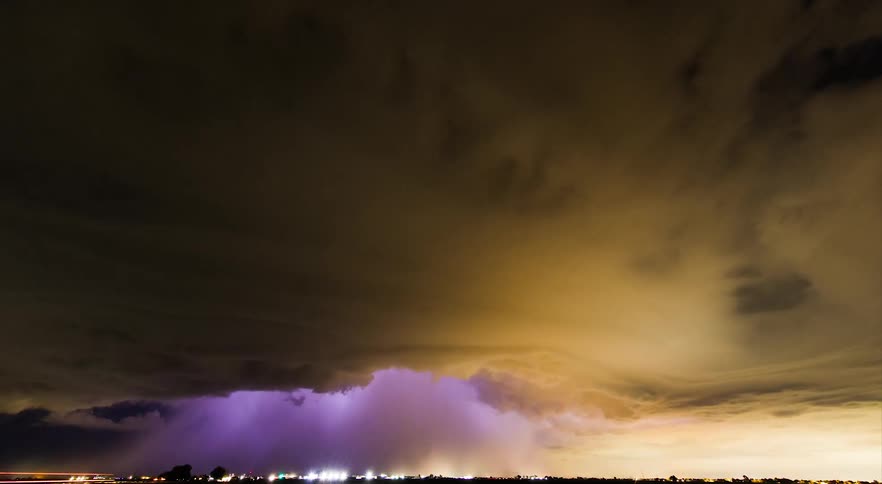 Dark yellow clouds move across the sky as purple lighting flashes like a strobe light inside the storm