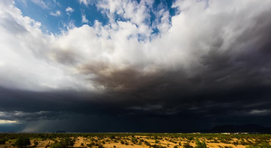 Storm clouds gather and flow across arid scrubland near mountains and kick up dust