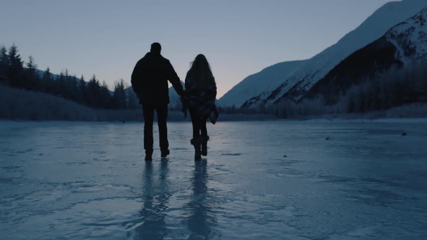 A couple walks across an icy pond