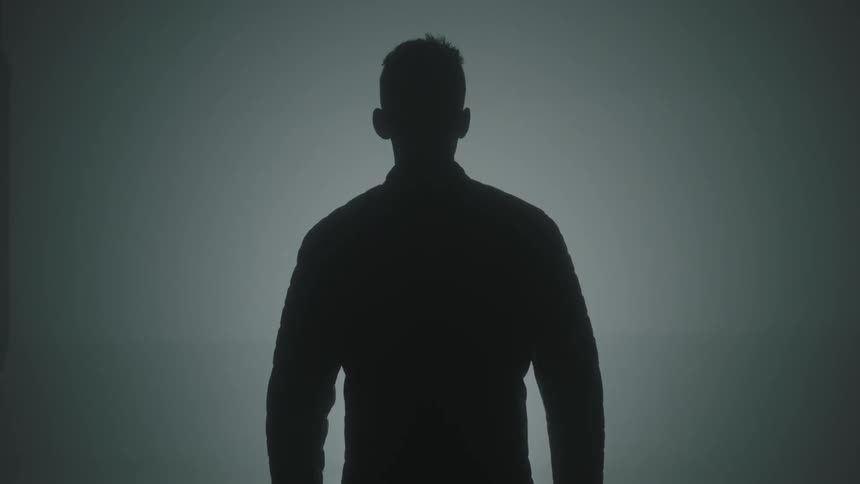 A man is standing still in a dimly lit place