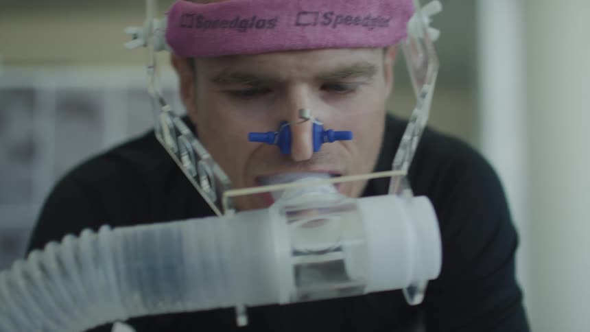 Medical technician adjusts breath apparatus as man pedals during medical test