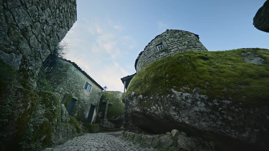 Moss covered stone walled buildings border cobblestone road in village