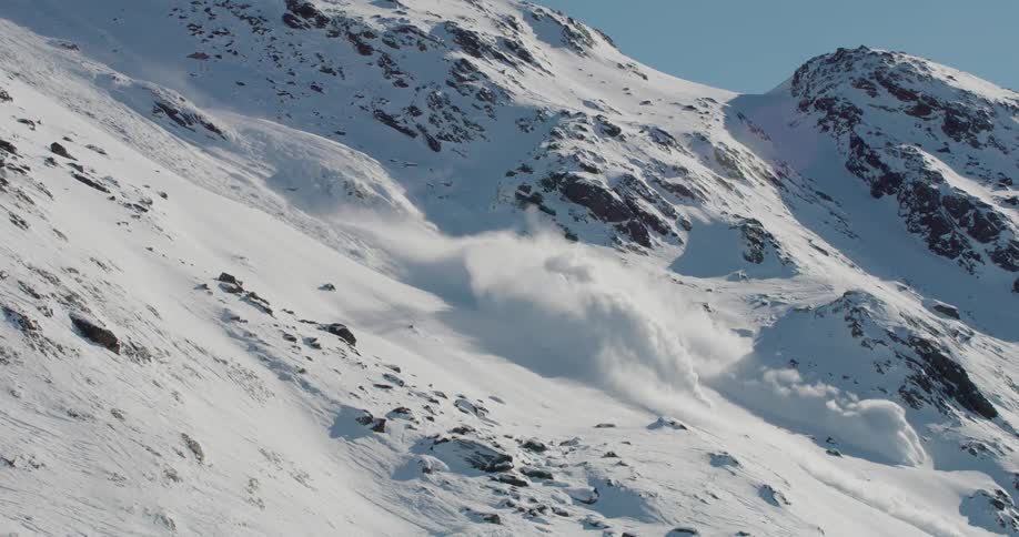 Snow falls down the side of a mountain during an avalanche