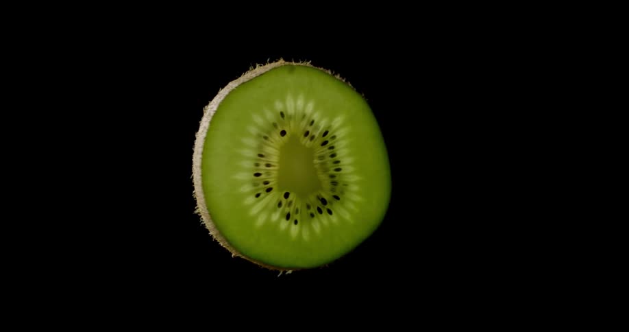Vibrant green slice of kiwi looking fresh and delicious while spinning in the darkness of a studio with cinematic lighting and colourful contrast