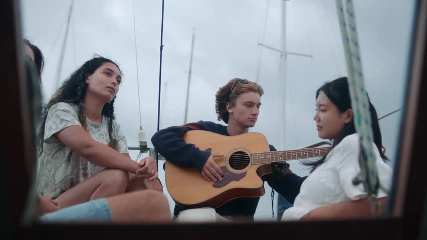 A man plays guitar on a boat as his friends sway to the music