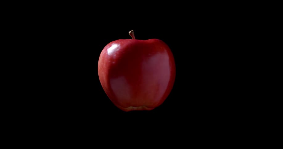 A fresh organic red apple fruit spins on its vertical axis in front of black background