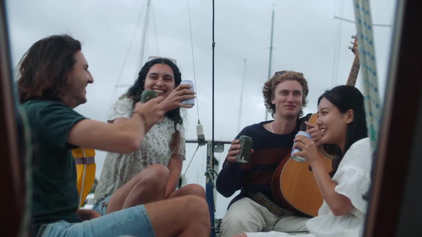 Friends sitting on sailboat toast each other then drink