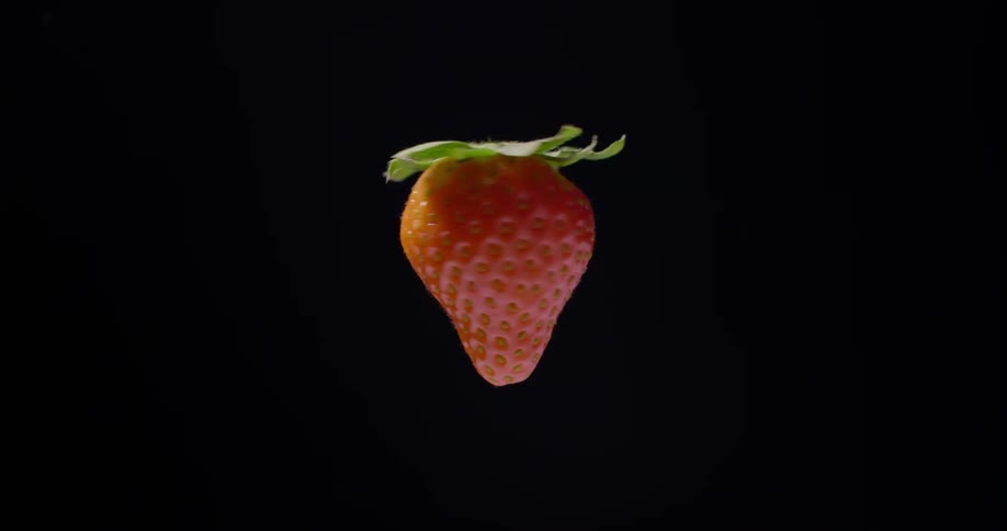 A fresh red strawberry is spinning around in the air looking delicious in front of a black background