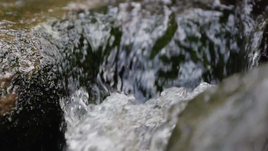 Water in a flowing stream splashes as it runs between rocks