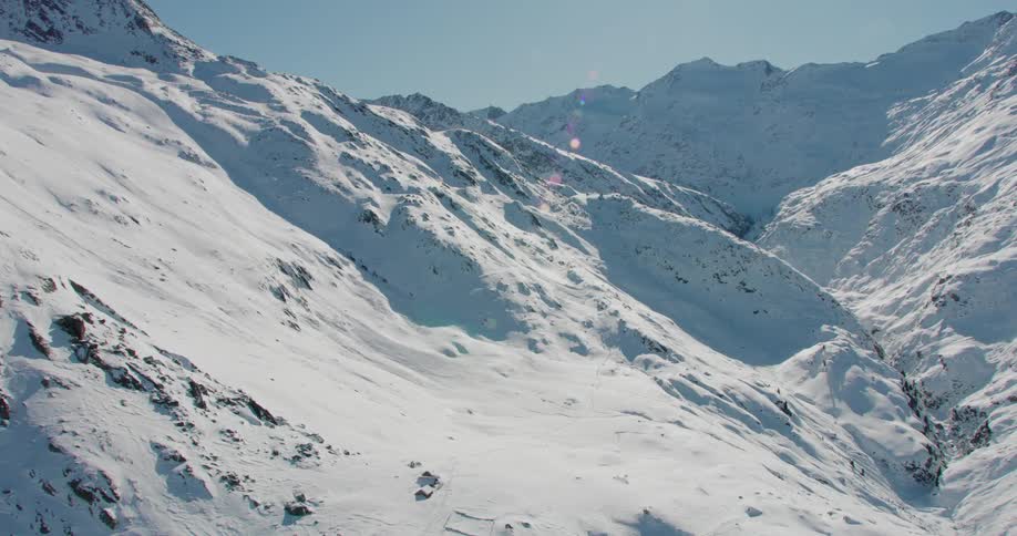 The sun shines brightly upon snow covered mountains under a clear sky on a winter day