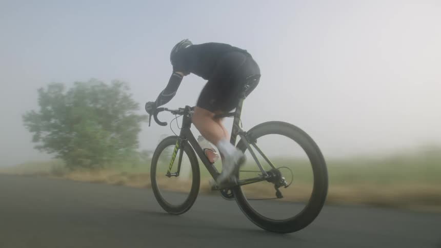 A bicyclist pedals down a foggy road