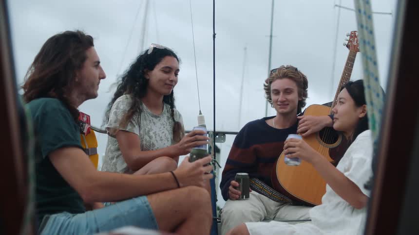 A group of friends sitting down and drinking from cans talks to each other laughing on boat