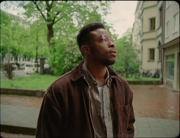 Man with glasses beard and brown jacket waits for woman on the street