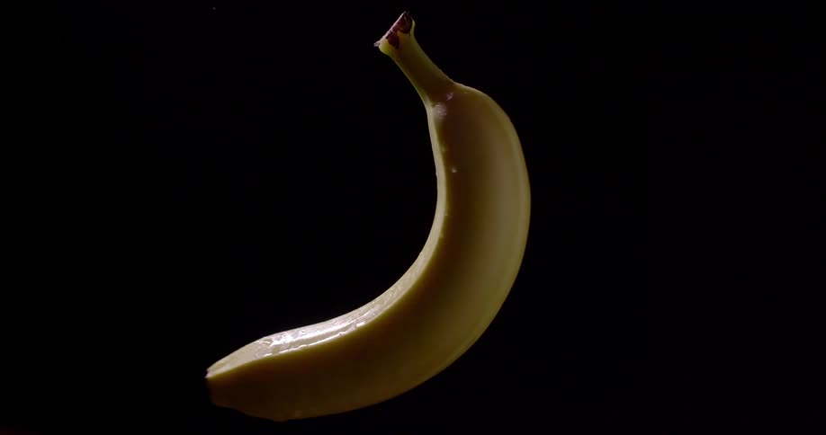 Yellow organic banana spins vertically in front of a black background ready to be eaten for a healthy meal with lots of vitamins