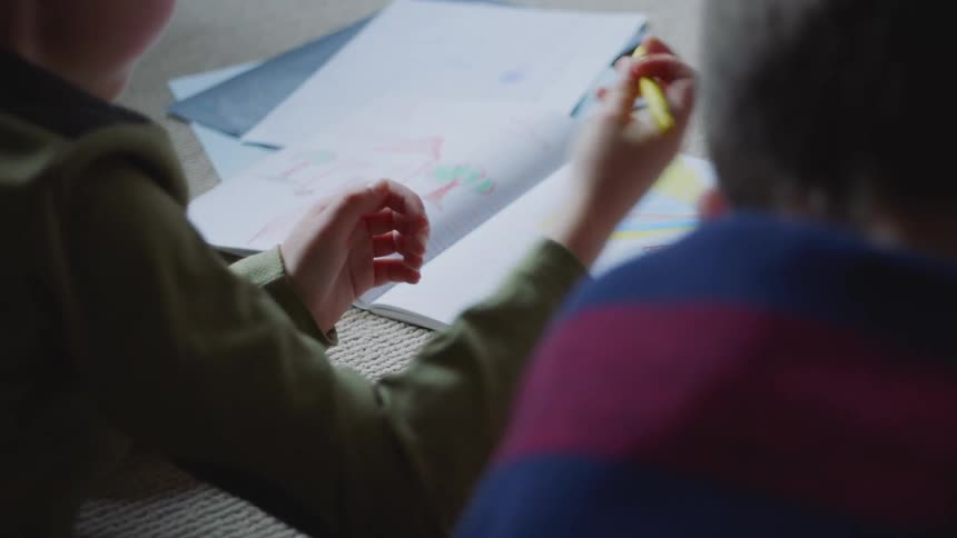 A couple of little boys drawing with crayons on the floor of a room