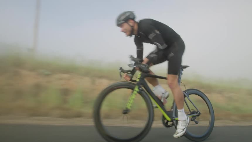 A man riding his bicycle is pedaling hard as he rides on a foggy rural road