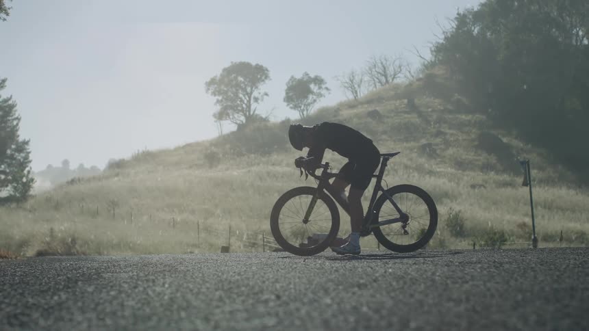 Biker rests on bike on the road next to hill
