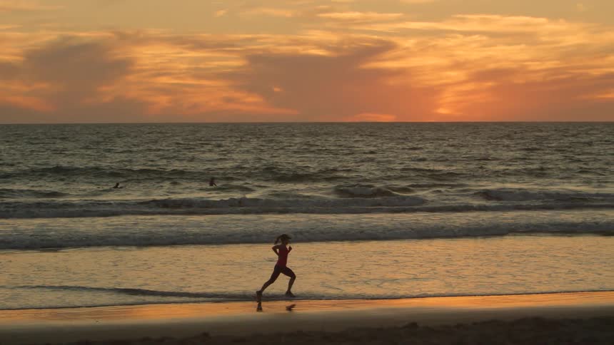 Woman running along beach in ocean silhouetted against the sunrise