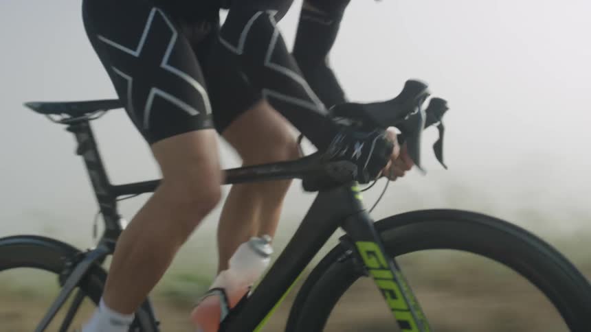 Cyclist with shorts and white sneakers and socks rides bicycle fast on the country road in fog